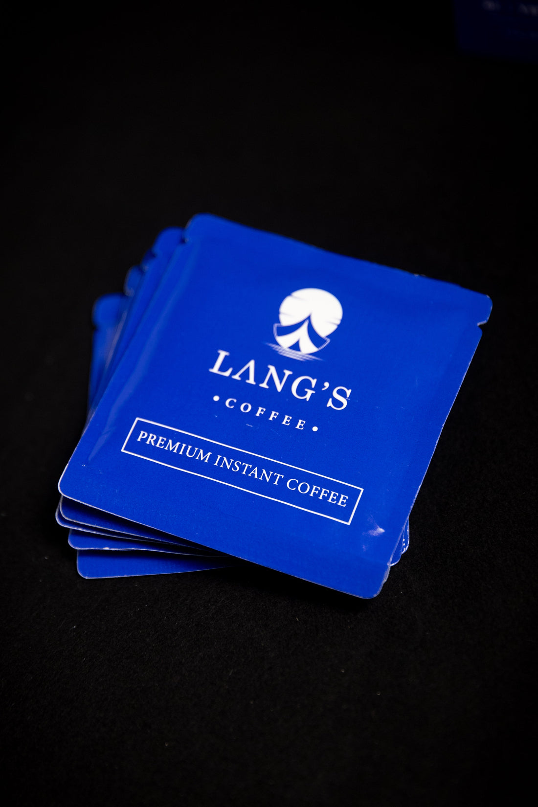 Stack of Lang's Coffee instant coffee packets on a dark surface